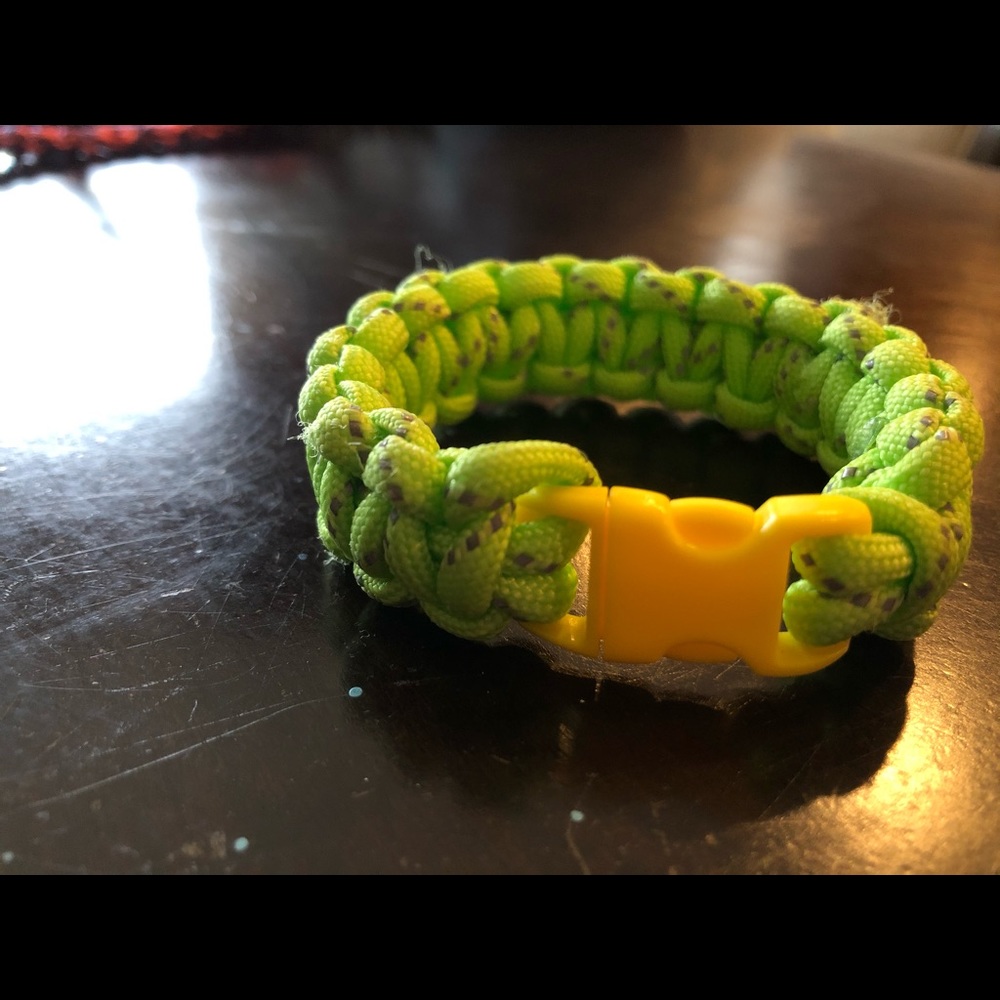 A green paracord rope bracelet with a yellow clip